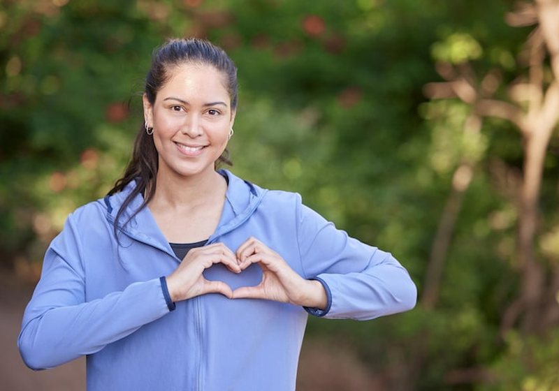 A woman making a heart shape with her hands during an outdoor workout